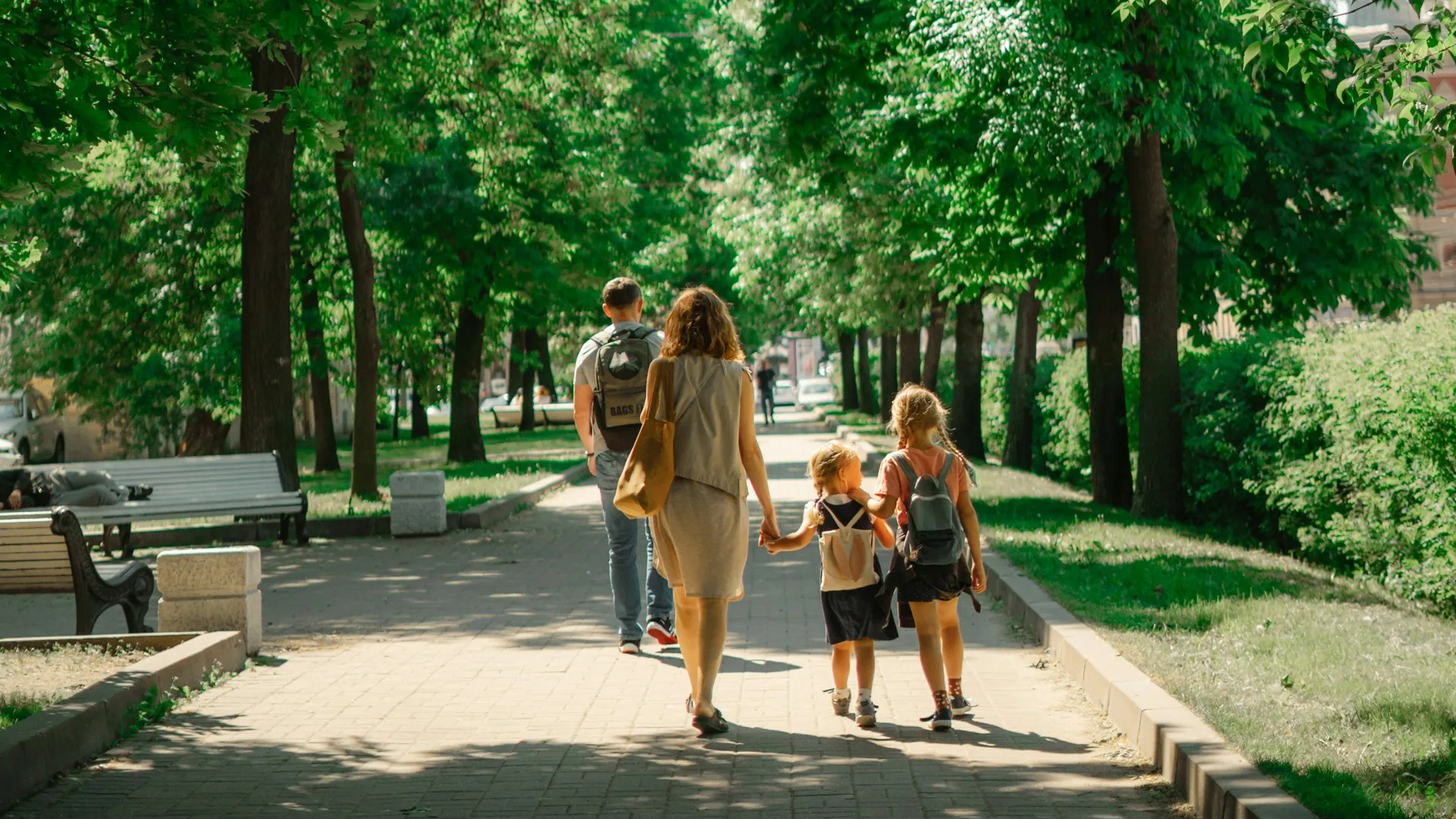 Une famille marche dans une allée bordée d'arbres, les enfants devant, sac au dos